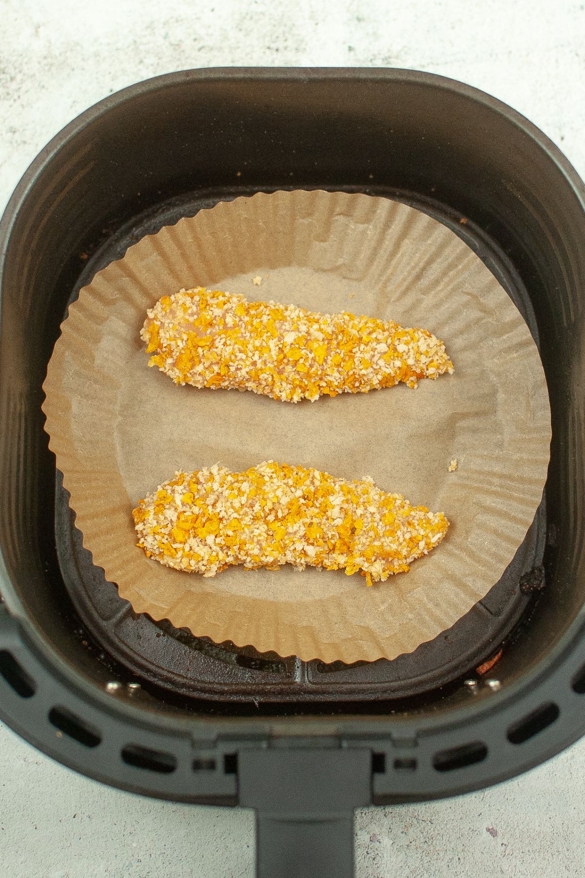 chicken tenders in an air fryer basket lined with parchment paper