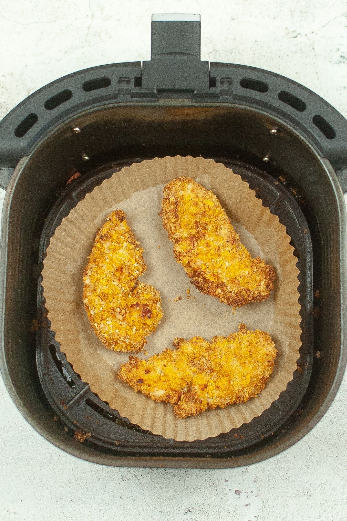 cooked chicken tenders in an air fryer basket lined with parchment paper