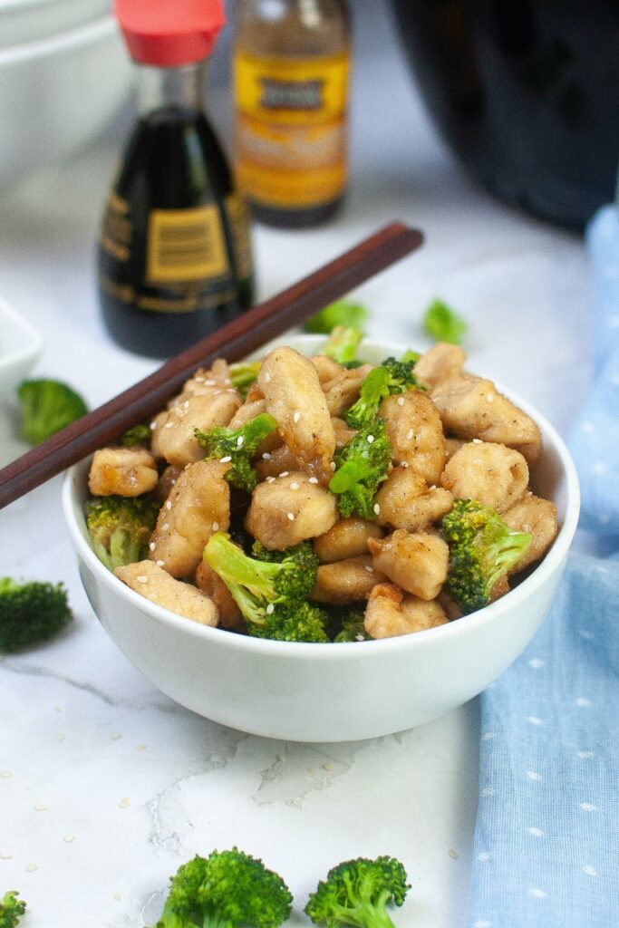 white bowl filled with air fryer chicken and broccoli with chopsticks on the top