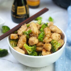 white bowl filled with chicken and broccoli with a pair of chopsticks on the top