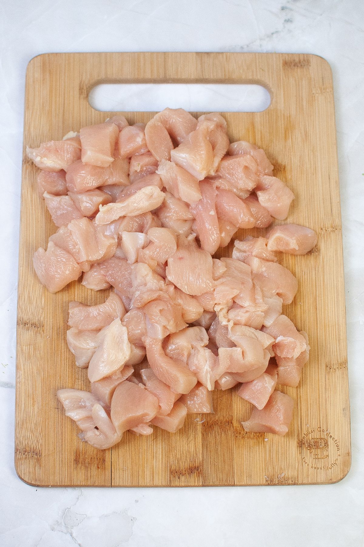 chicken breast cut into chunks on a wooden cutting board