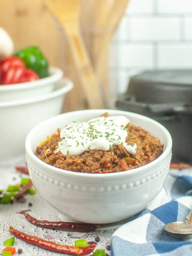 white bowl filled with dutch oven chili topped with sour cream and fresh parsley