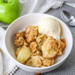 white bowl filled with apple cobbler with a scoop of vanilla ice cream