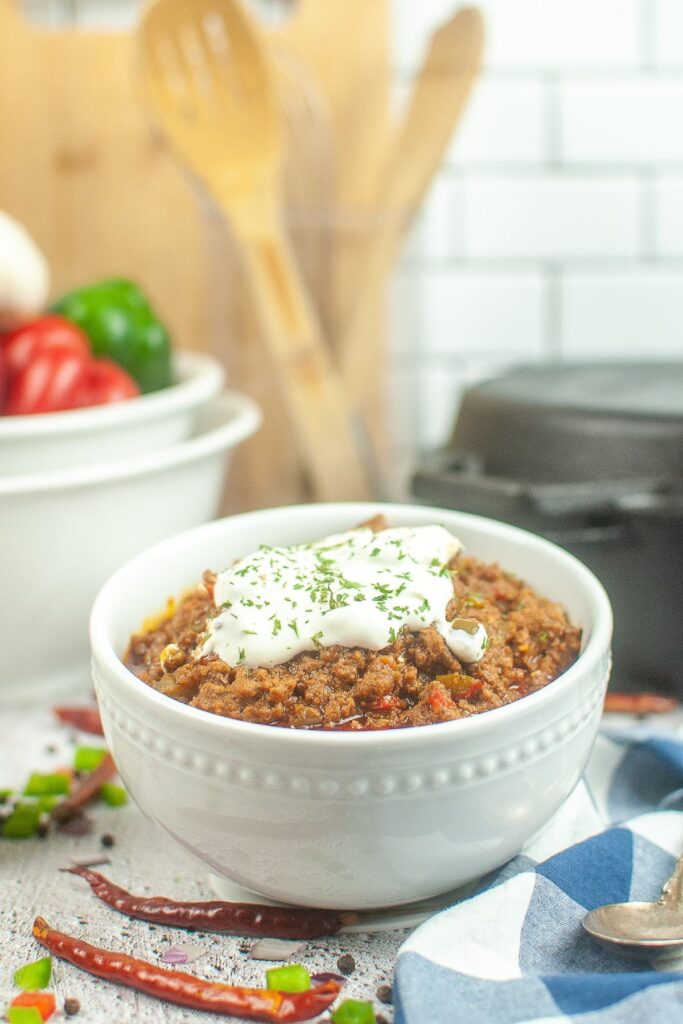 white bowl filled with dutch oven chili topped with sour cream and fresh parsley