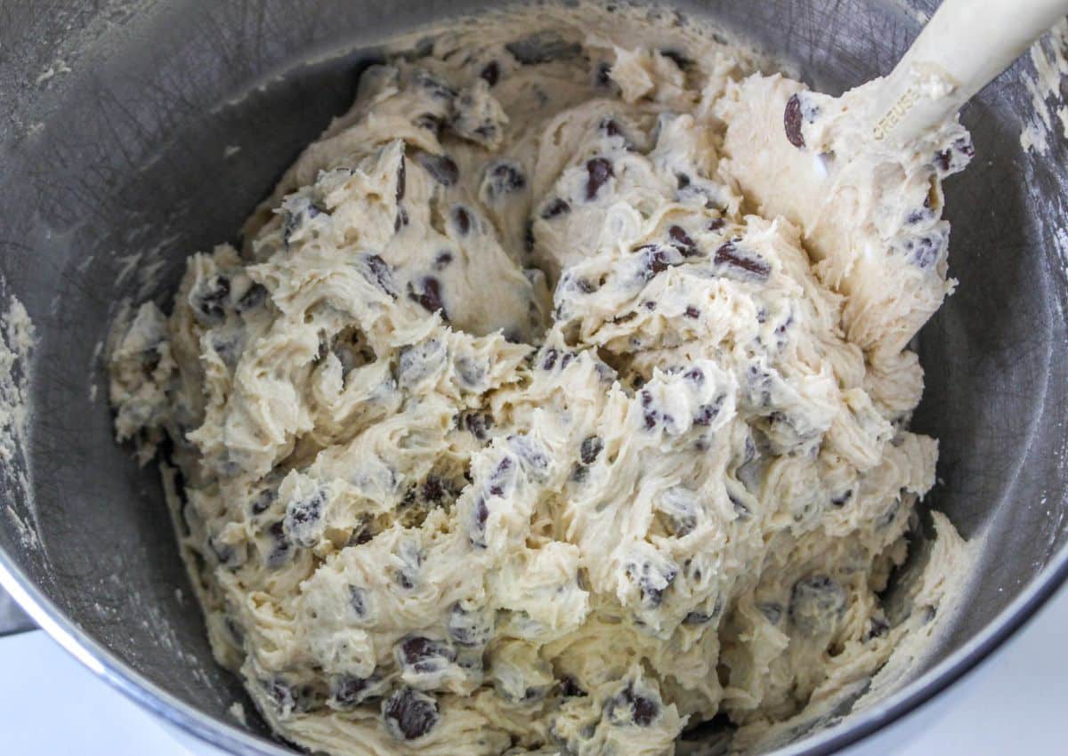 chocolate chips being adding to a mixing bowl full of dough