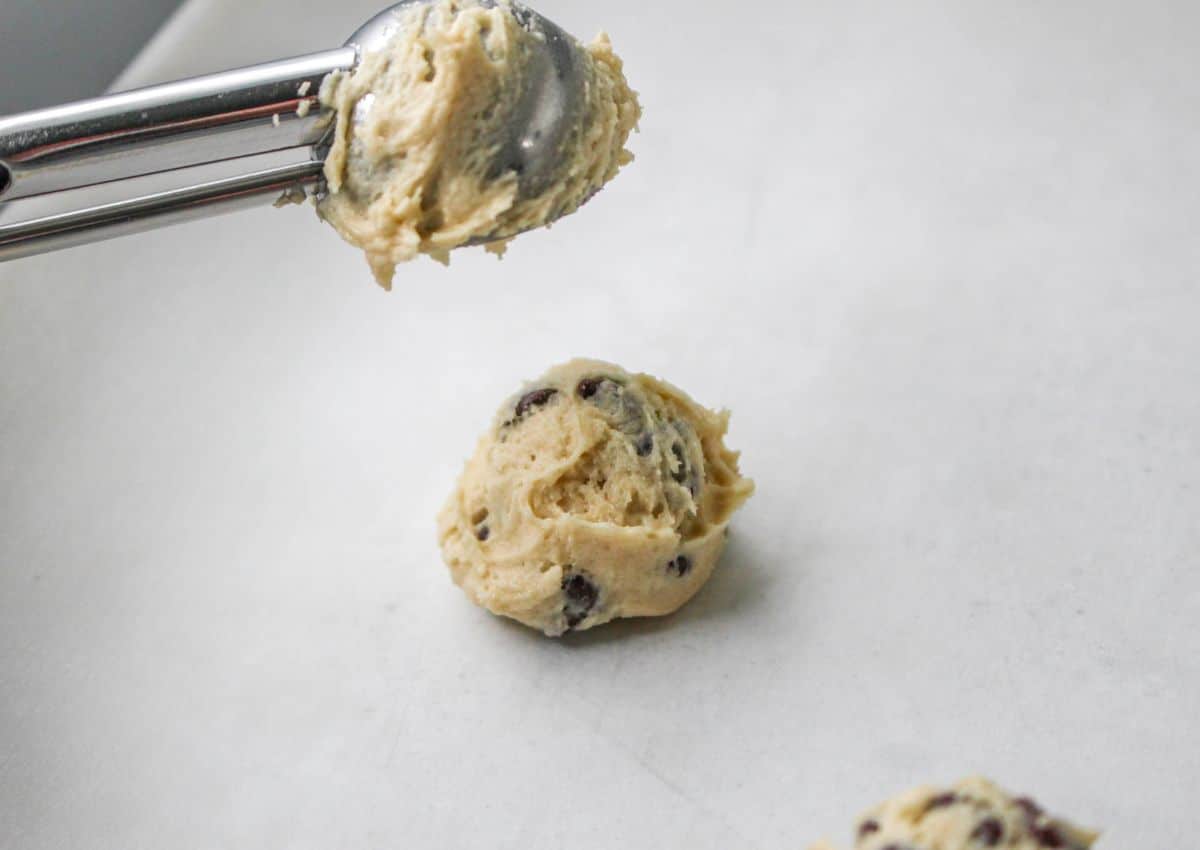 cookie scoop shaping dough balls onto a parchment lined baking sheet