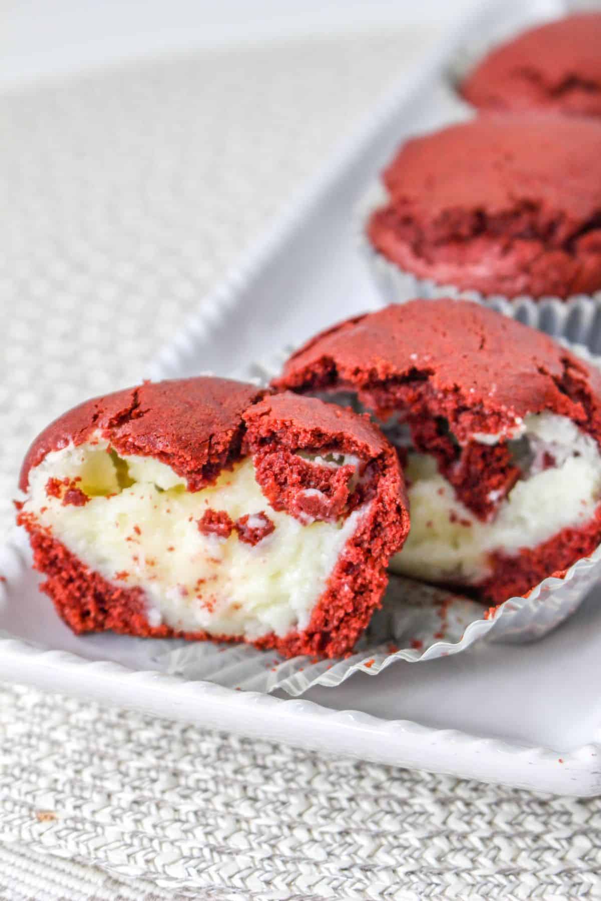 red velvet muffins on a white platter with one split open to show the cream cheese filling inside.