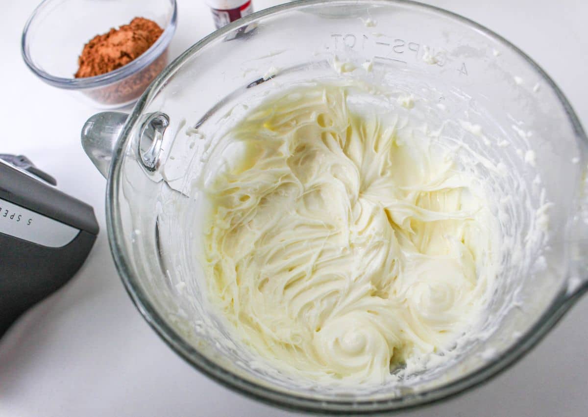 cream cheese and powdered sugar being mixed in a glass mixing bowl