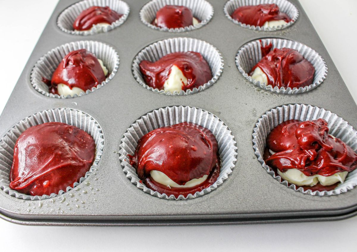 red velvet muffin batter being added to cupcake liners in a muffin pan