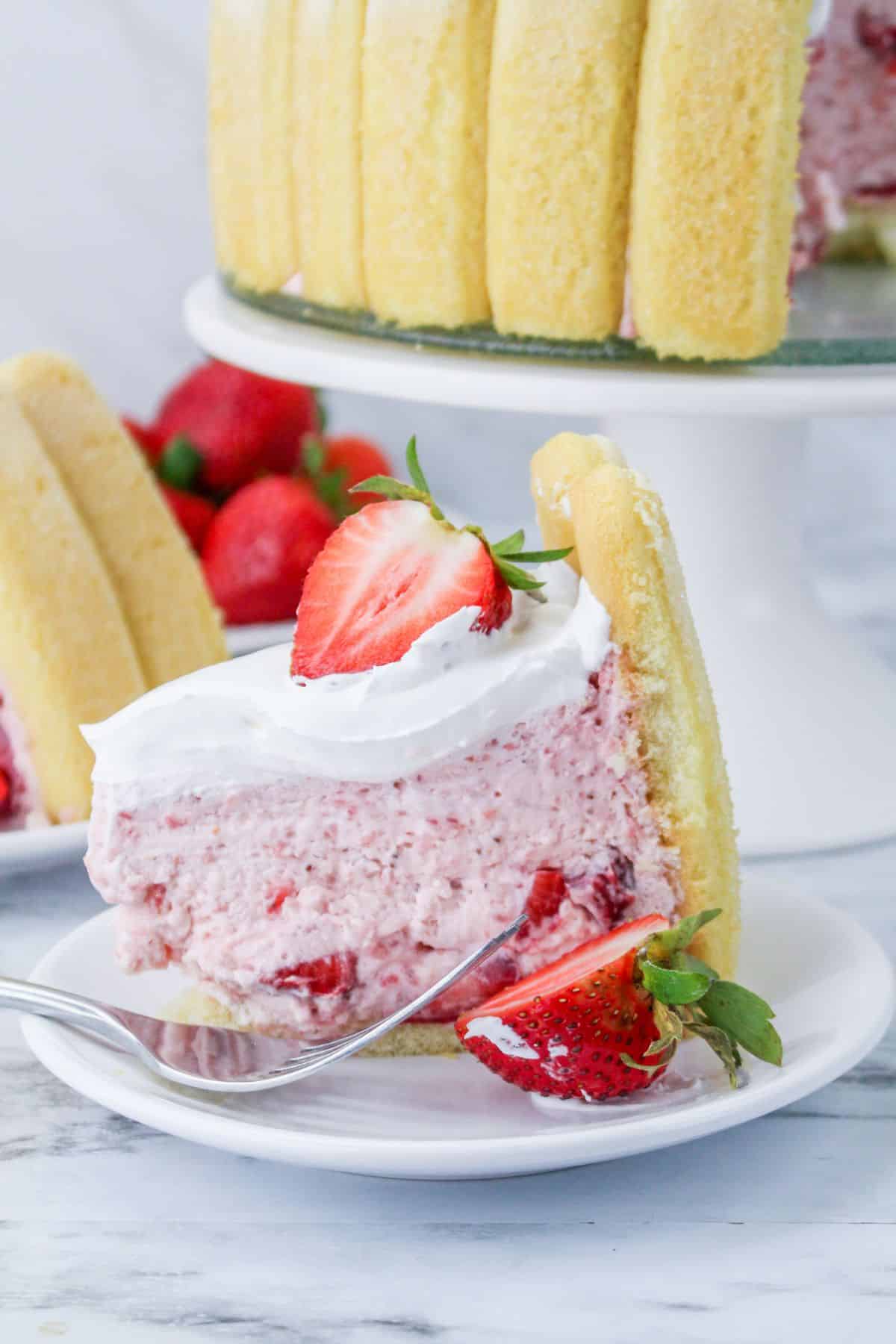 slice of strawberry charlotte cake on a white plate with a strawberry half