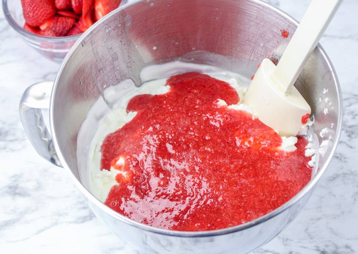 whipped cream being mixed with strawberry puree in a mixing bowl