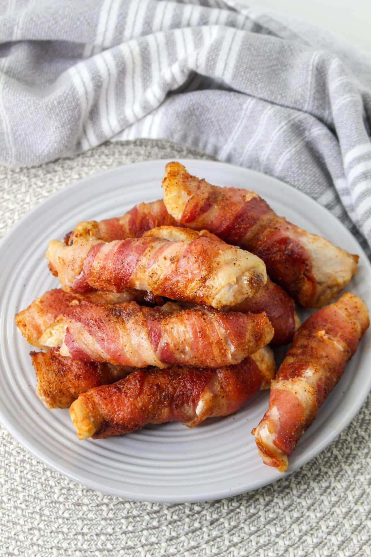 light gray plate stacked with bacon wrapped chicken tenders with a gray and white napkin in the background