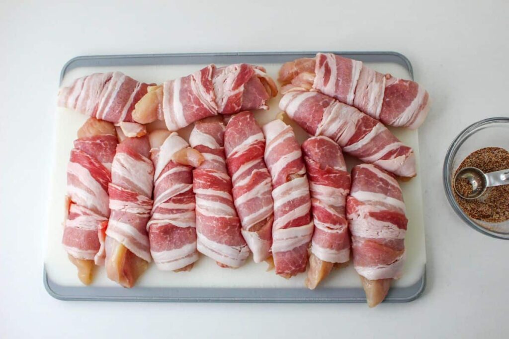 raw bacon wrapped around chicken tenders on a cutting board