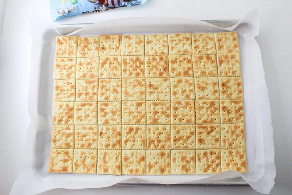 saltine crackers on a parchment lined baking sheet