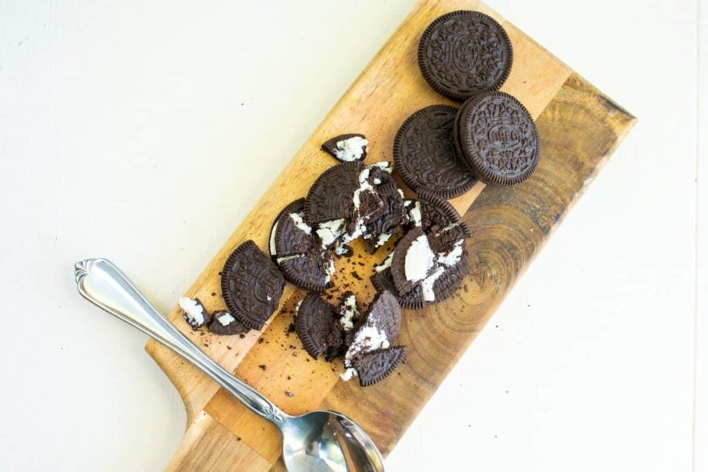 oreo cookies being broken up on a wooden cutting board