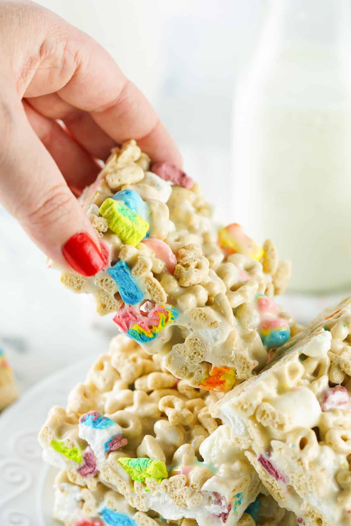 a woman's hand with red finger nails removing a lucky charms treat from a white plate