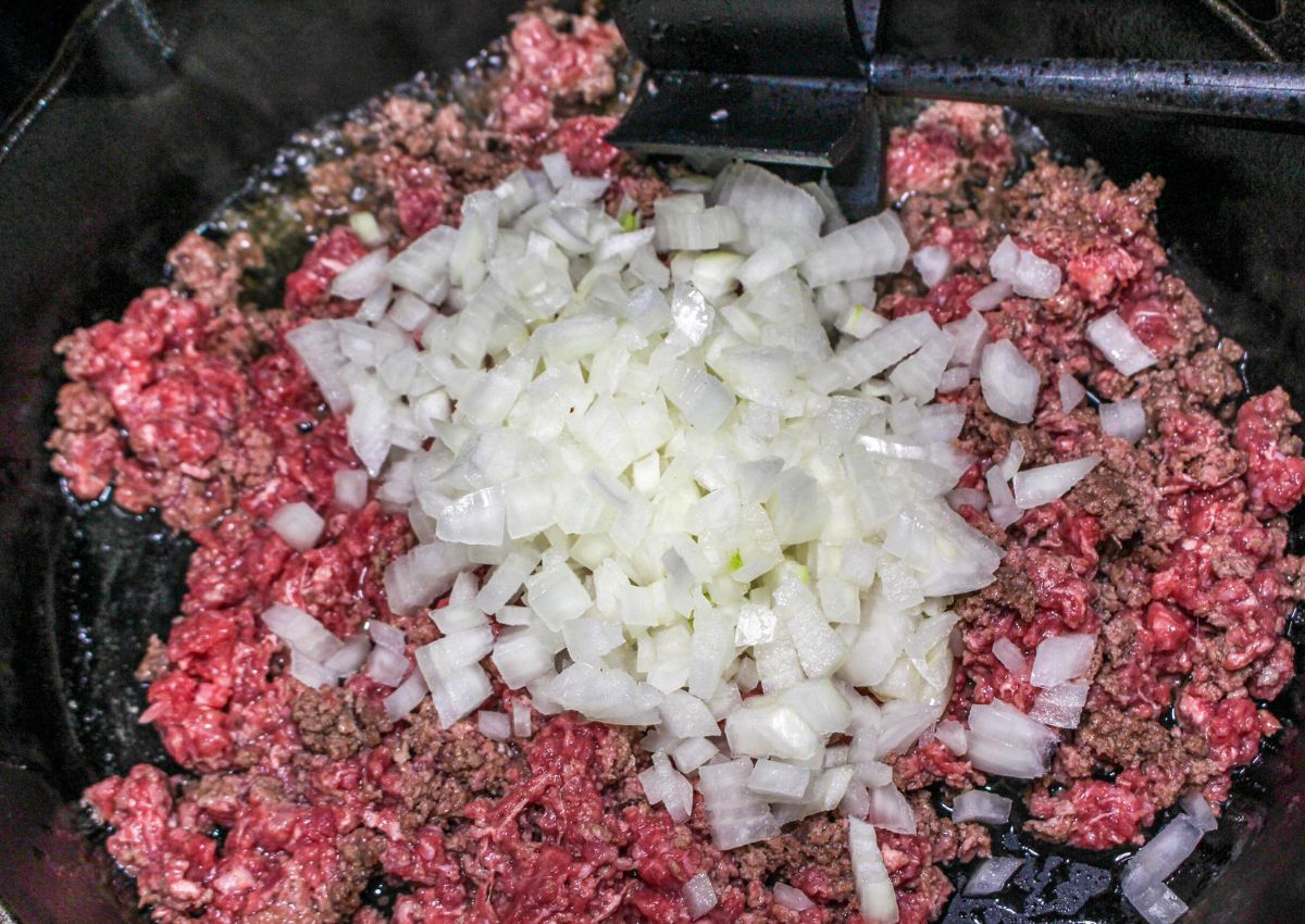 ground beef and onions being cooked in a cast iron skillet