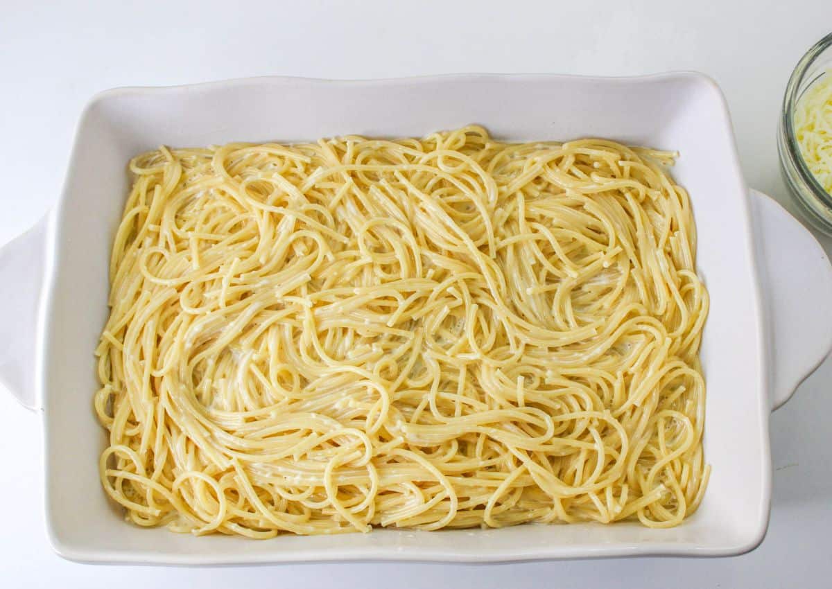 cooked spaghetti noodles mixed with alfredo sauce in a white baking dish