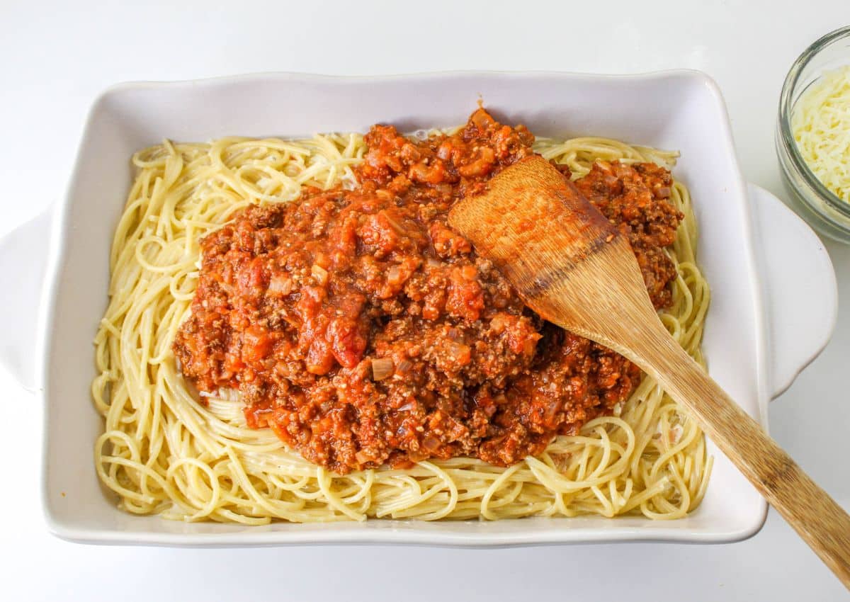 meat sauce being spread on top of pasta noodles.