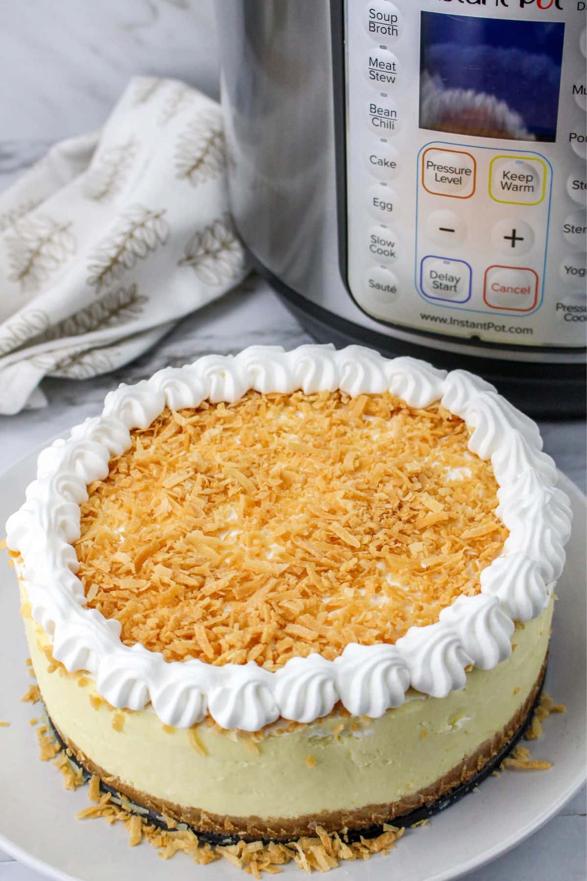 whole uncut cheesecake on a white plate with a pressure cooker in the background