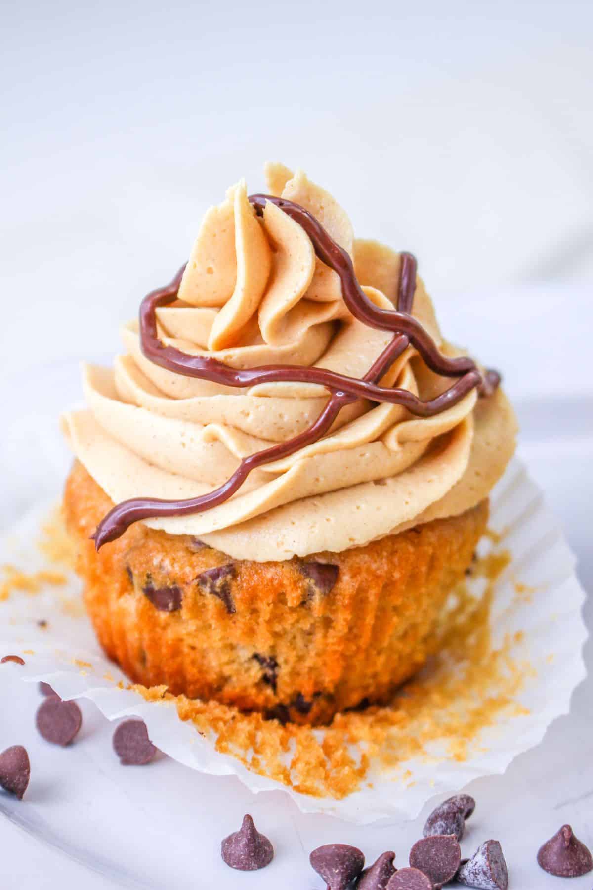 chocolate chip cupcake with the liner unwrapped on a white plate with chocolate chips sprinkled around