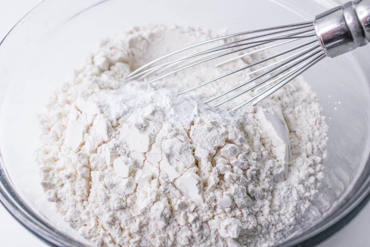 flour, salt, and baking powder being whisked in a glass mixing bowl