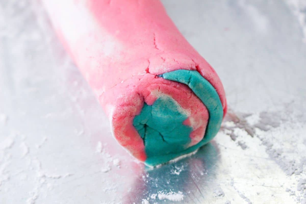 pink and blue cookie dough being shaped into a log