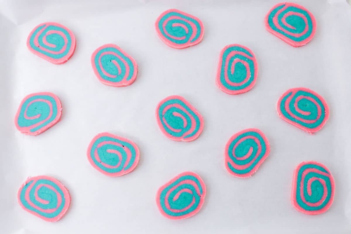 unbaked pink and blue swirled cookies on a parchment lined baking sheet