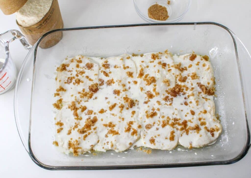 biscuits topped with heavy cream and brown sugar in a glass casserole dish