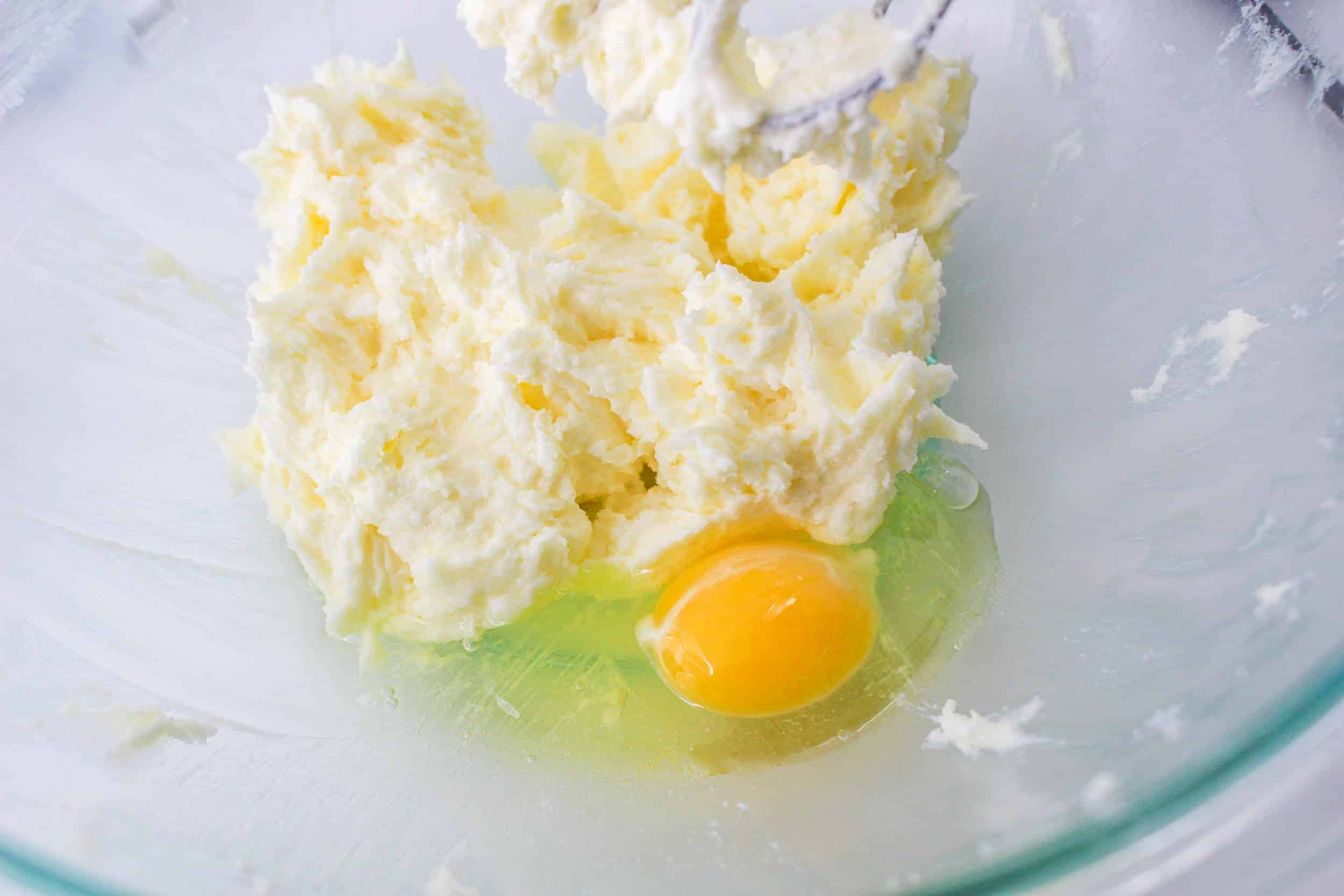 egg being added butter and sugar in a glass bowl.