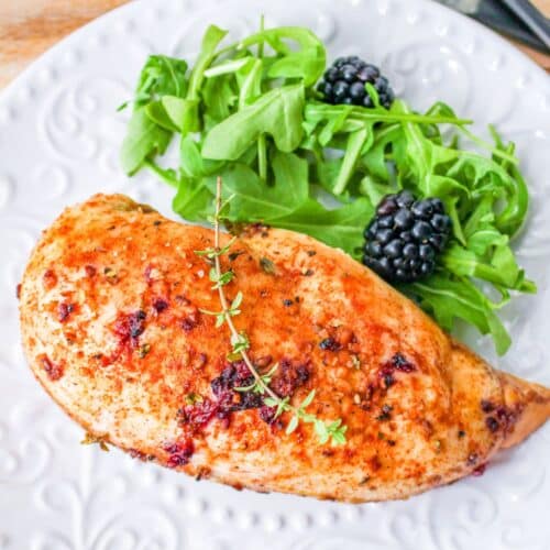 blackberry chicken breasts on a white plate with a bed of spring mix and fresh blackberries