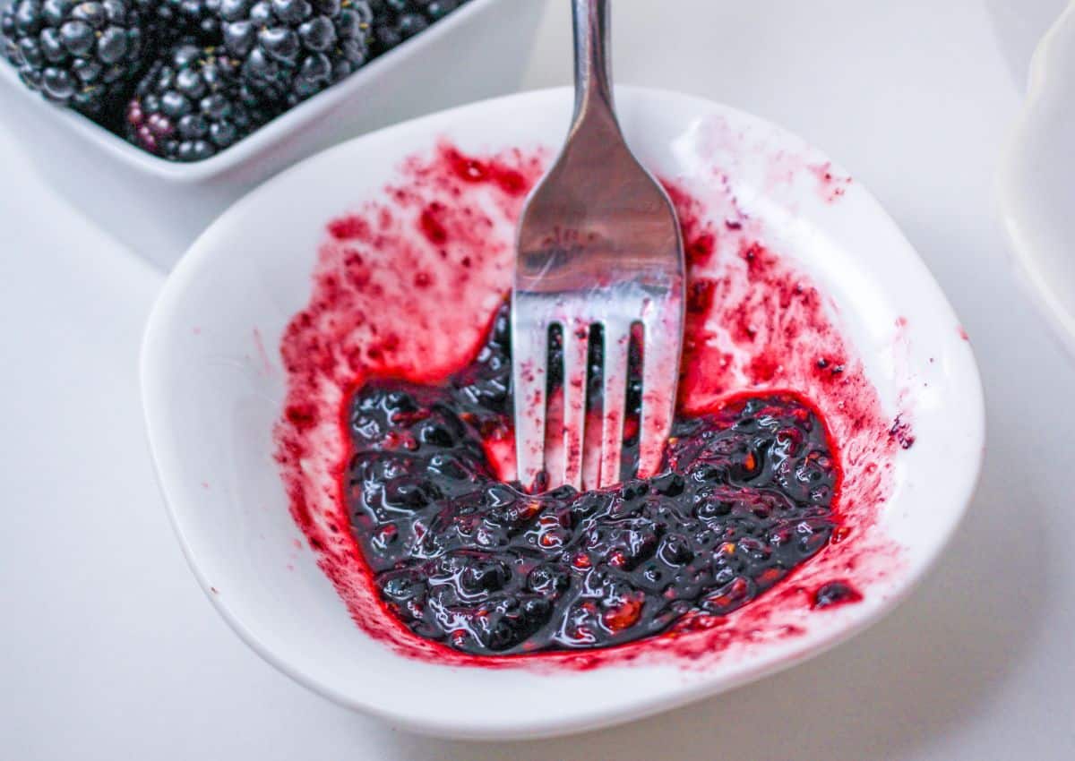 blackberries being mashed with a fork in a small white bowl