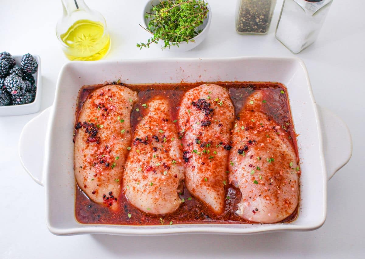 raw chicken breasts topped with seasonings and blackberry marinade in a white baking dish