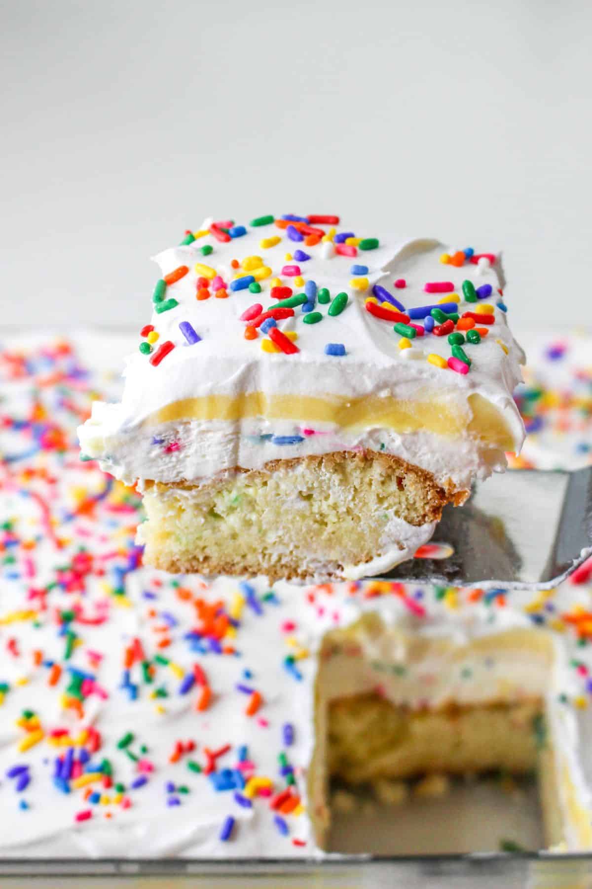 slice of funfetti lush on a stainless steel spatula over baking dish filled with the lush