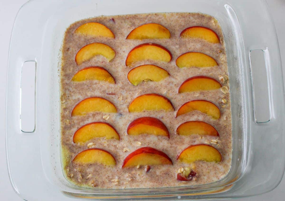 raw baked oatmeal meal batter topped with fresh peach slices in a glass baking dish