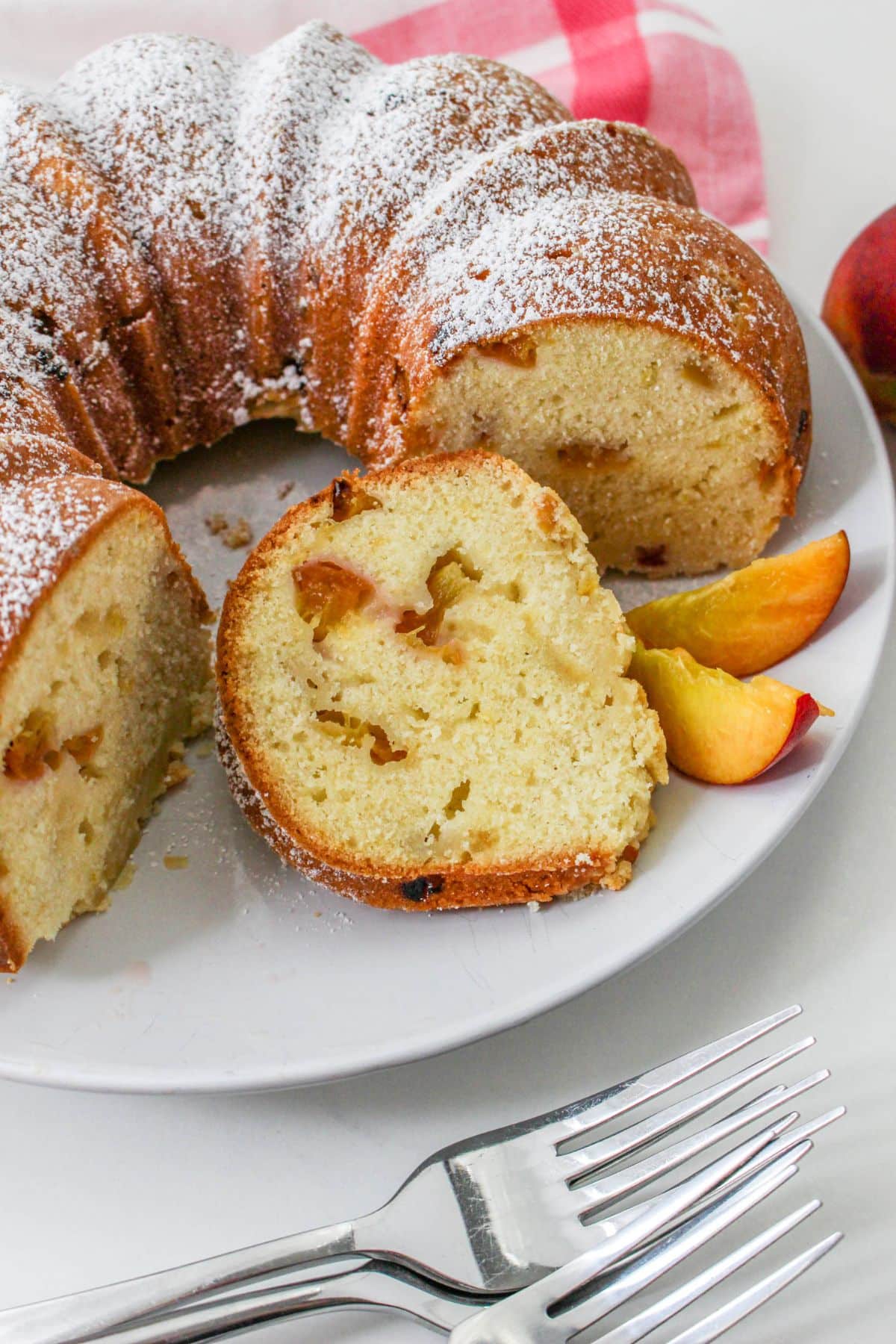 whole pound cake sliced on a white plate with sliced peaches around it