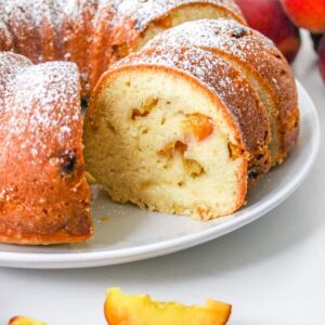 whole pound cake sliced on a white plate with sliced peaches around it