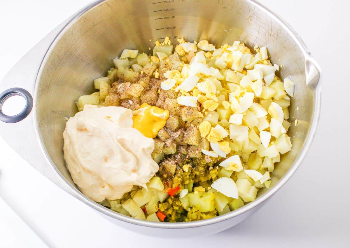 potato salad ingredients being mixed in a stainless steel mixing bowl