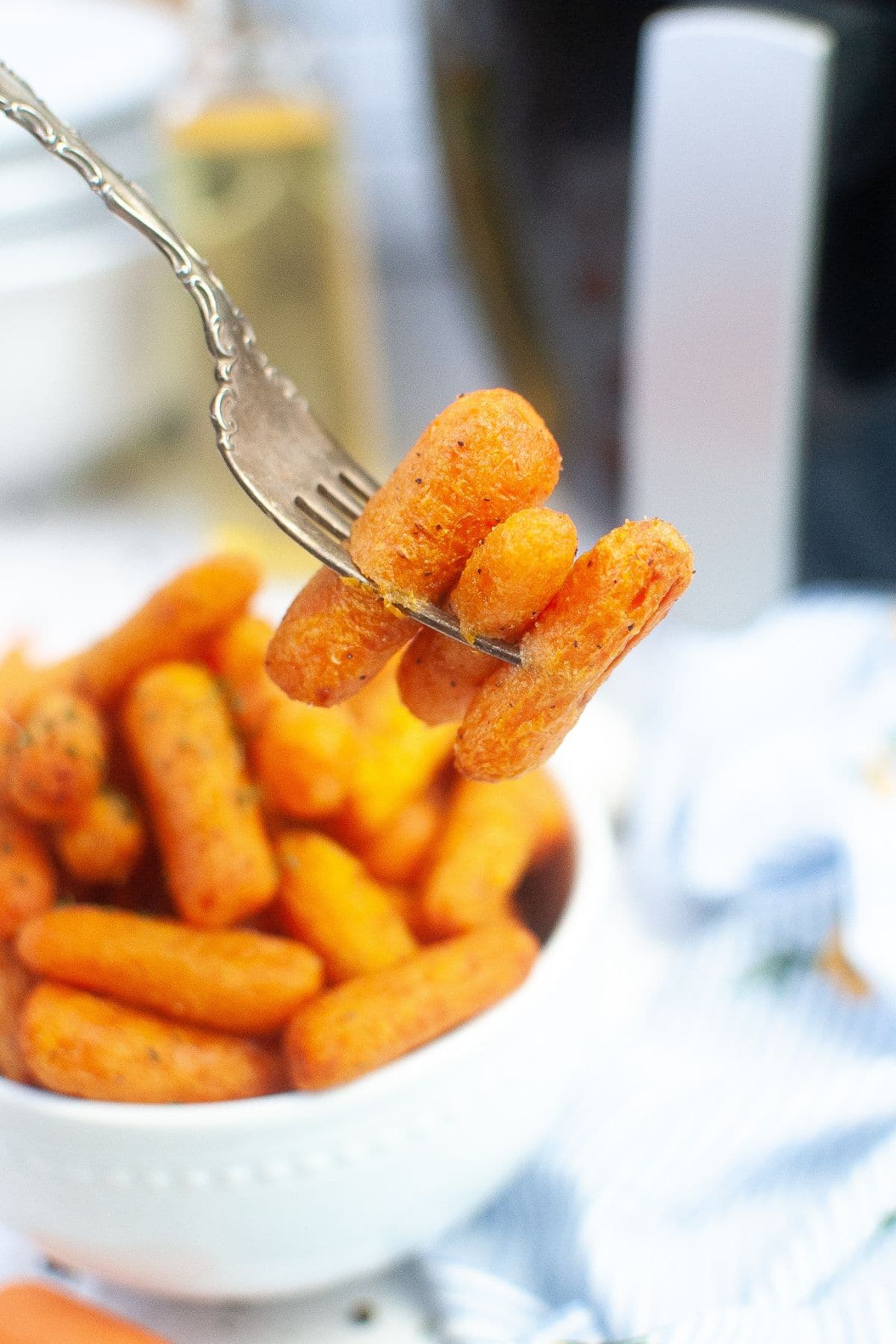 three baby carrots on a sliver fork with the rest in a white bowl in a background