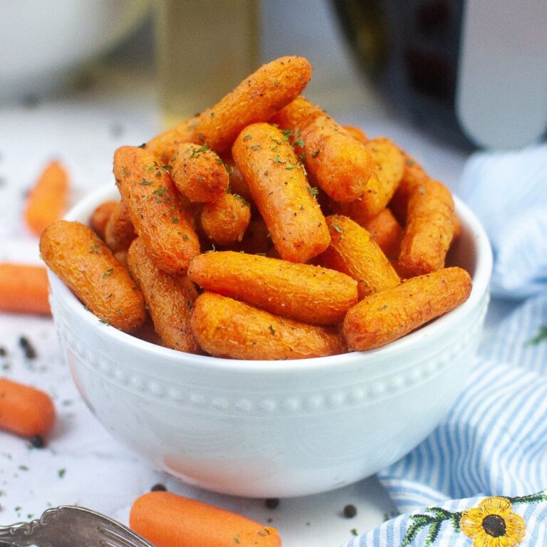 white bowl filled with air fryer baby carrots with a air fryer in the background