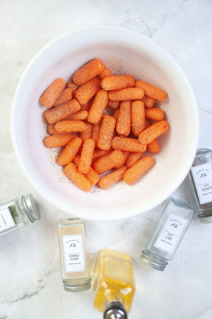 raw carrots in a large white bowl with oil and seasonings being seasoned on