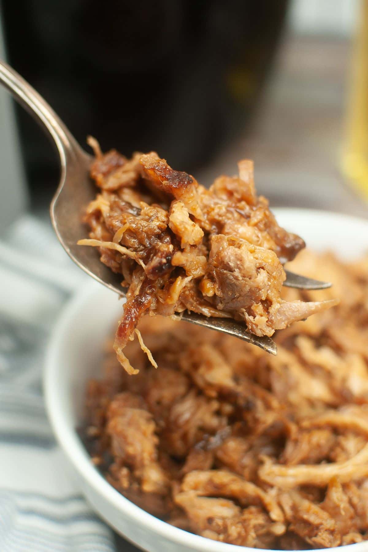 bite of pulled pork held on a large stainless steel fork in the air above a white bowl