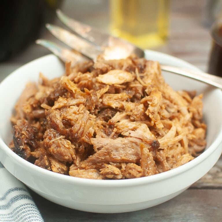 white bowl filled with pulled pork with a large sliver fork on the back of the bowl