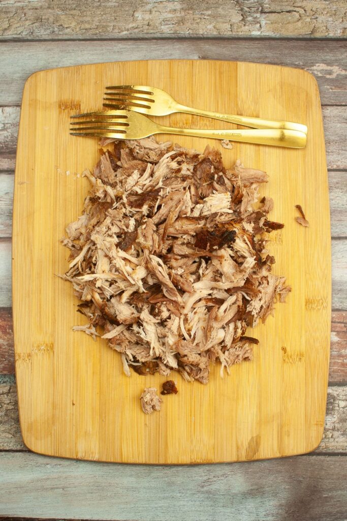 shredded pork on a wooden cutting board with two golden forks