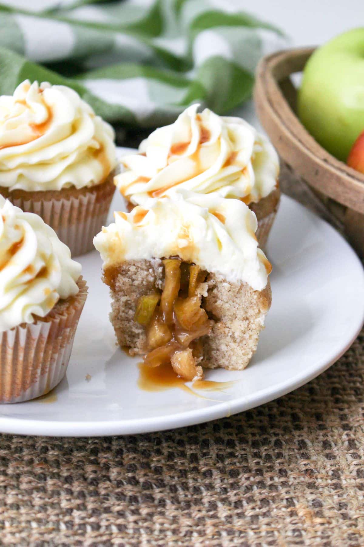 four apple pie cupcakes on a white plate with one cut open to show the pie filling inside
