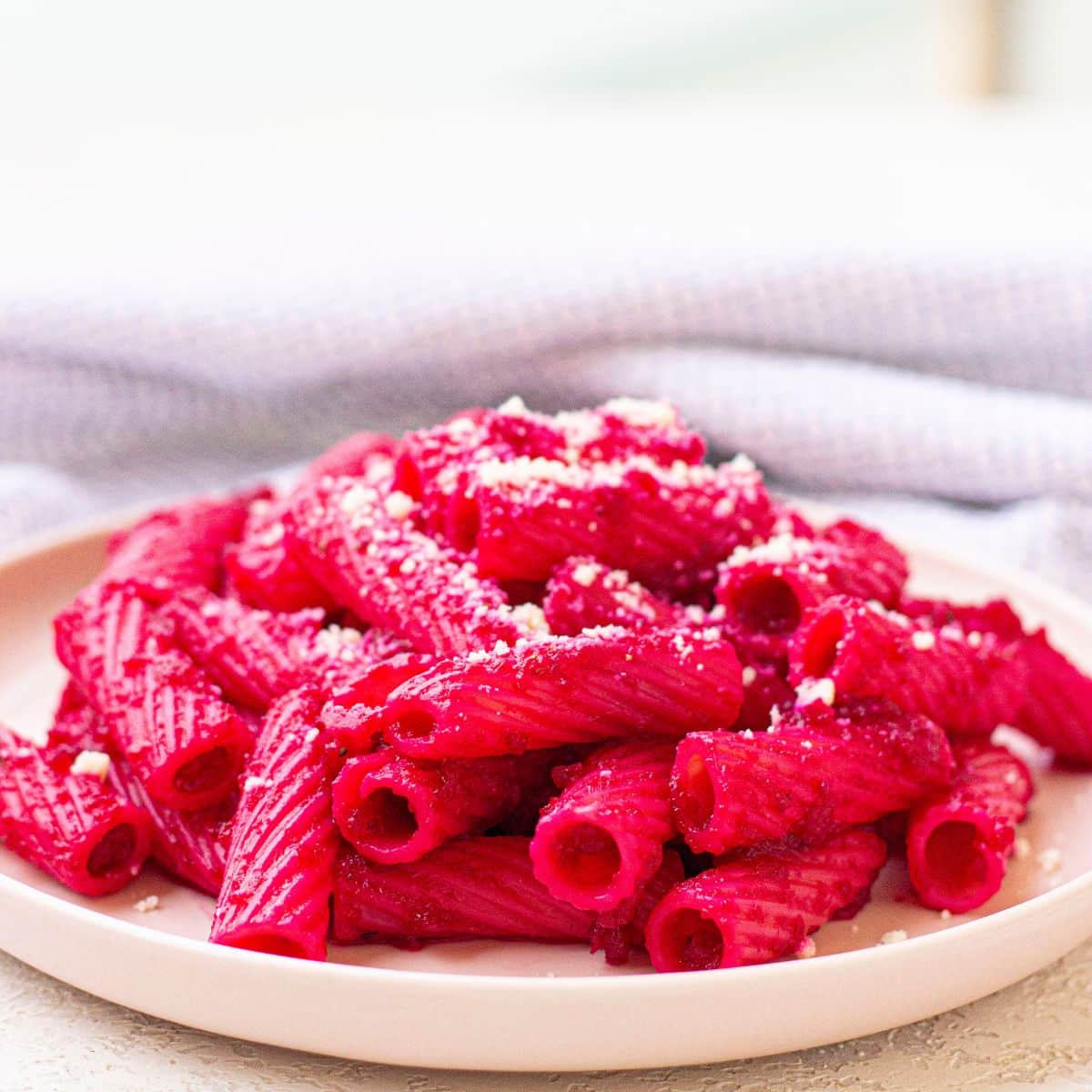 white plate with deep sides filled with beetroot pasta topped with parmesan cheese