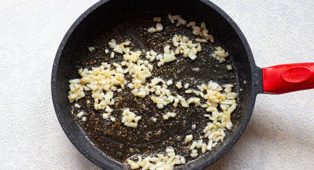 onions being sauteed in a skillet with melted butter