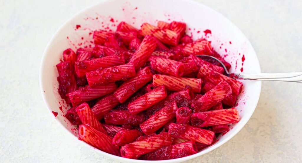 cooked pasta being tossed in beet pasta sauce in a white bowl