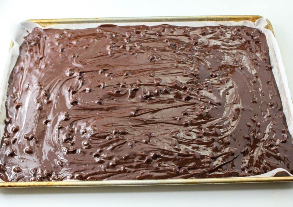 brownie batter being spread in a jelly roll pan that is lined with parchment paper