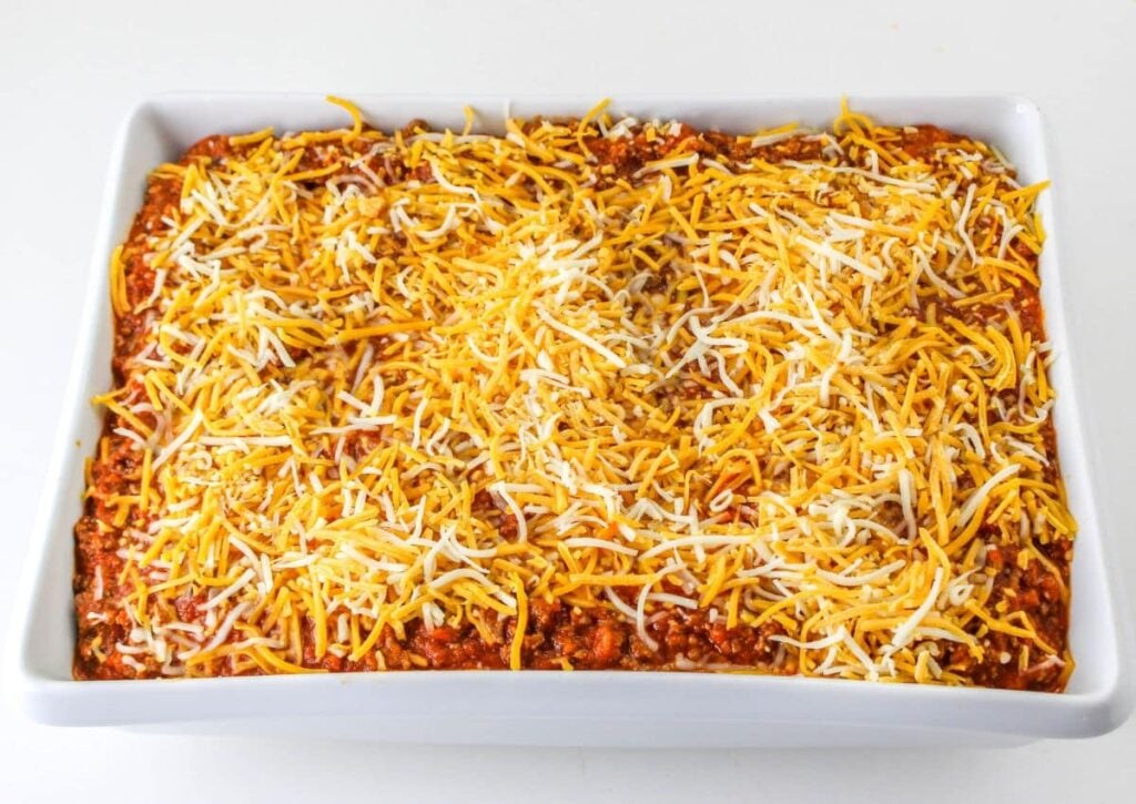 garlic bread casserole topped with shredded cheese in a white casserole dish ready to go in the oven